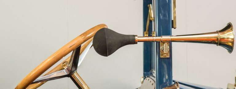 The front of a vintage blue car with an antique golden steering wheel and a separate horn