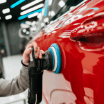 Mécanicien en train de polir la carrosserie d’une voiture dans un atelier professionnel.