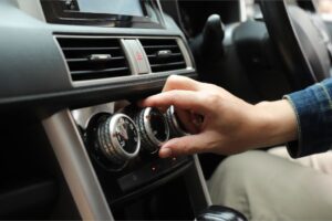 Técnico a inspecionar o sistema de ar condicionado de um veículo numa oficina, com ferramentas e equipamento de diagnóstico visíveis.