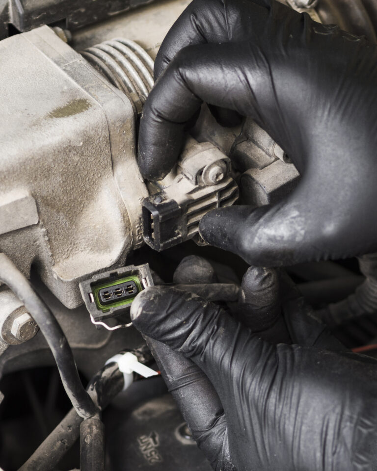 Técnico a inspecionar conectores e derivações elétricas de um veículo numa bancada de oficina, com ferramentas de diagnóstico ao lado.