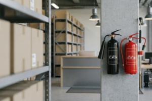Extintores de CO2 e de água dispostos numa oficina, com sinalização de segurança e equipamento de proteção visível.