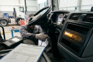 Técnico de flotas en un taller conectando un equipo de diagnosis a un camión para revisar datos del tacógrafo inteligente, con un portátil mostrando parámetros y un lector de tarjetas en la mesa.