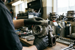 Professionnel d’un garage automobile manipulant ou installant un turbo en échange standard dans un atelier.