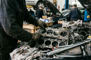 Technicien automobile en train d’intervenir sur un joint de culasse dans un atelier, dans un contexte technique lié au temps de réparation et à la rentabilité.