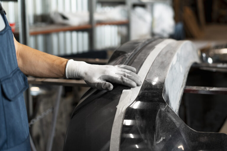 Profesional de automoción revisando o instalando un recambio de carrocería con precisión en un taller especializado.