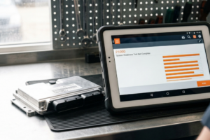 Módulo de control del motor (ECU) en un banco de trabajo junto a un escáner que muestra el código P1000 System Readiness Test Not Complete.