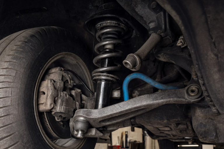 Vista detallada del sistema de suspensión delantera de un coche montado, incluyendo el amortiguador con muelle, brazo de suspensión, rótula y barra estabilizadora azul.