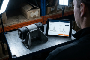 Suporte Motor Opel Astra H 1.7 CDTI: Vibração, Km e Preço Real B2B PT 3 Operario analizando un soporte de motor silentblock en un banco de trabajo con una tablet que muestra gráficos de frecuencia de vibración.