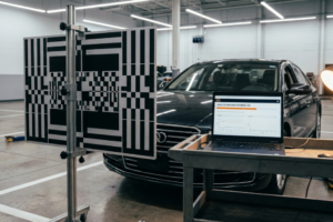 Panel de patrones geométricos para calibración de sistemas ADAS frente a un vehículo Audi con ordenador en progreso.