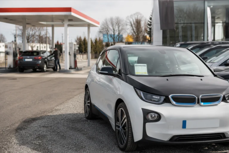 Coche eléctrico BMW i3 blanco y negro estacionado cerca de una estación de servicio