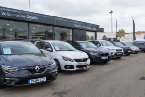 Exposición de coches de ocasión y kilómetro cero alineados frente a un concesionario.