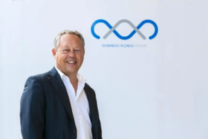 Hombre con traje sonriendo frente al logotipo de Domingo Alonso Group.