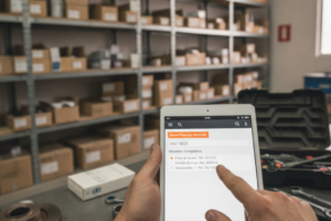 Mãos de um mecânico a utilizar um tablet para pesquisar peças compatíveis por matrícula num armazém de peças auto.