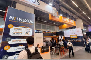 Stand d'exposition de l'entreprise Nexus Automotive Aftermarket lors d'un salon professionnel avec des visiteurs et des panneaux d'information.