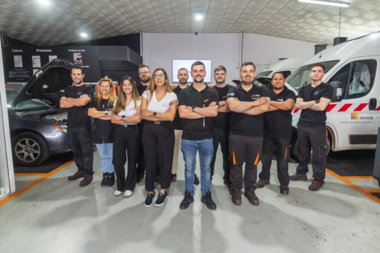 Grupo de empleados y mecánicos posando sonrientes de brazos cruzados dentro del taller mecánico con vehículos al fondo.