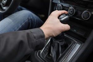 Mecânico com luvas pretas segurando a manopla de câmbio manual no interior de um carro desmontado