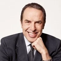 Primer plano del rostro de un hombre adulto de cabello oscuro vistiendo trajes corporativos.