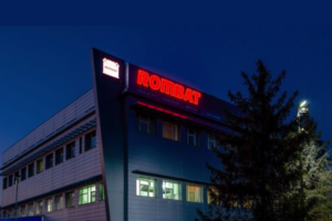 Façade du bâtiment de l'usine Rombat avec enseigne lumineuse rouge de nuit.